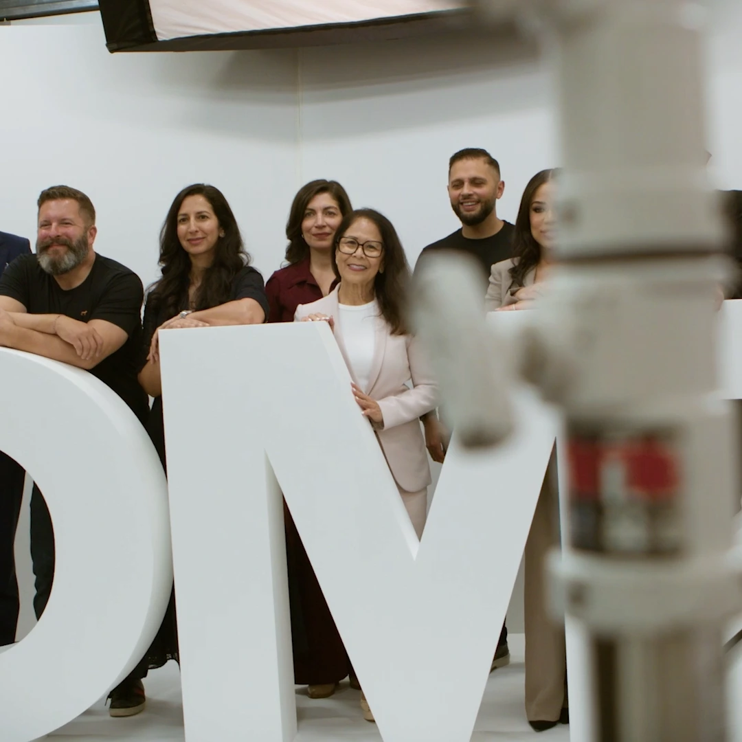 Six members of the DMZ team standing behind large white sculpted DMZ letters in a bright studio